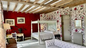 A bedroom with a four-poster bed, a sofa, a desk with a lamp, and floral wallpaper.