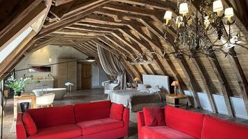 Un acogedor dormitorio en el ático con techo inclinado, vigas de madera, un candelabro, un sofá rojo y una cama con cabecera blanca.