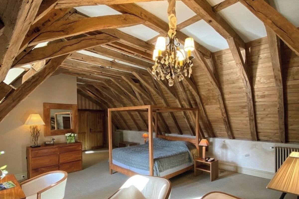 A spacious attic bedroom with exposed wooden beams, a four-poster bed, and a chandelier.