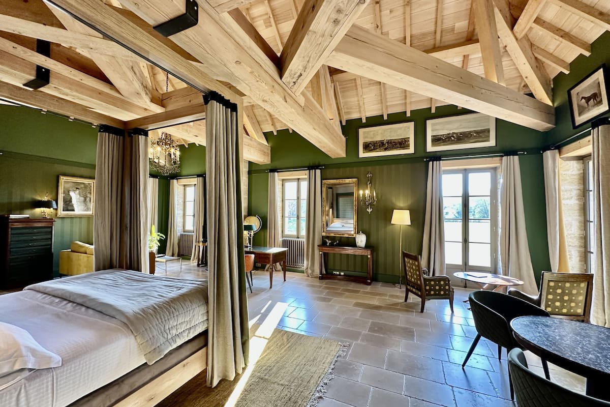 A room with a high wooden ceiling, a bed, a desk, chairs, and a table.