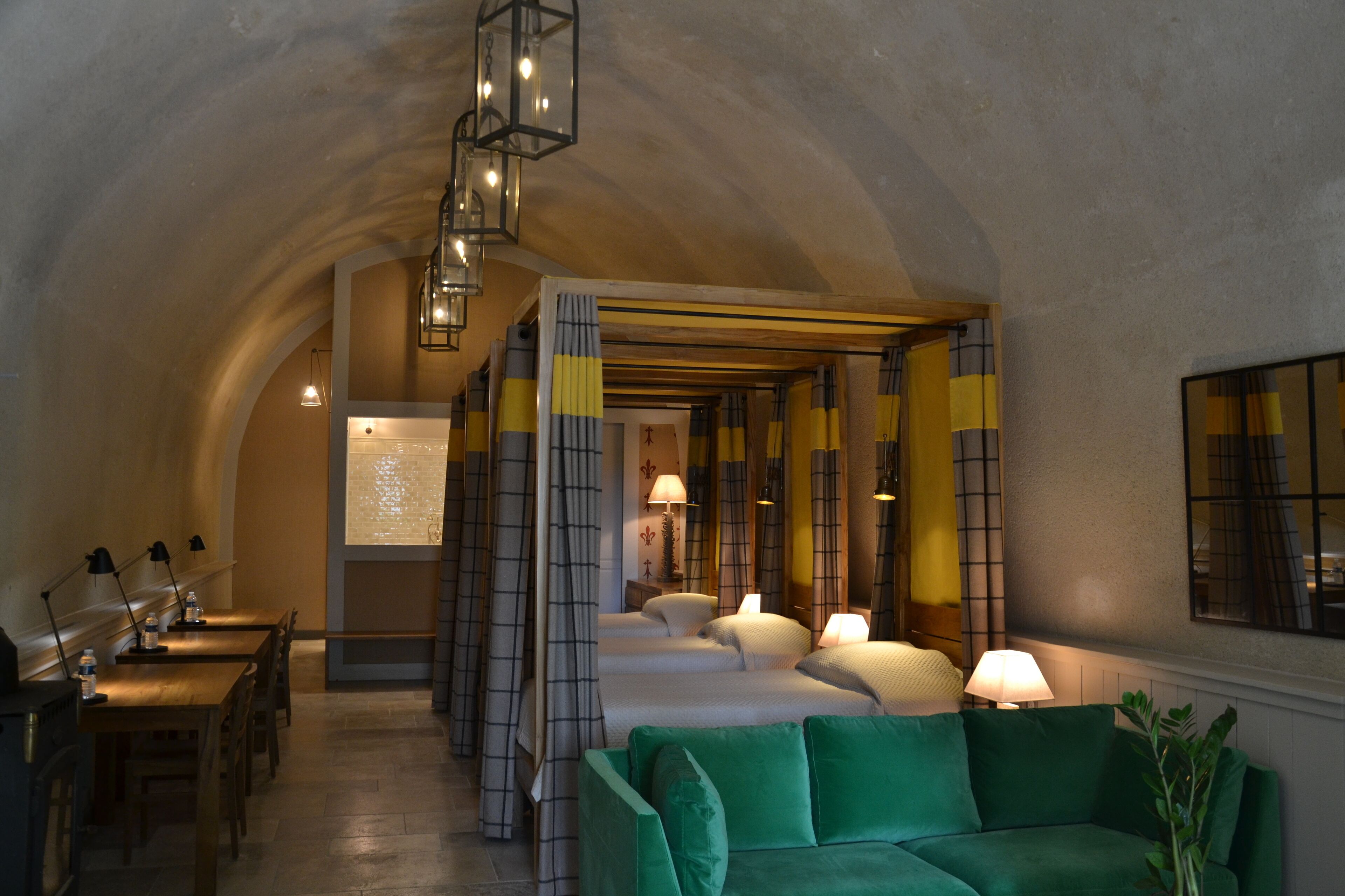A cozy hotel lobby with a green sofa, wooden tables, and a staircase leading to a bedroom area.