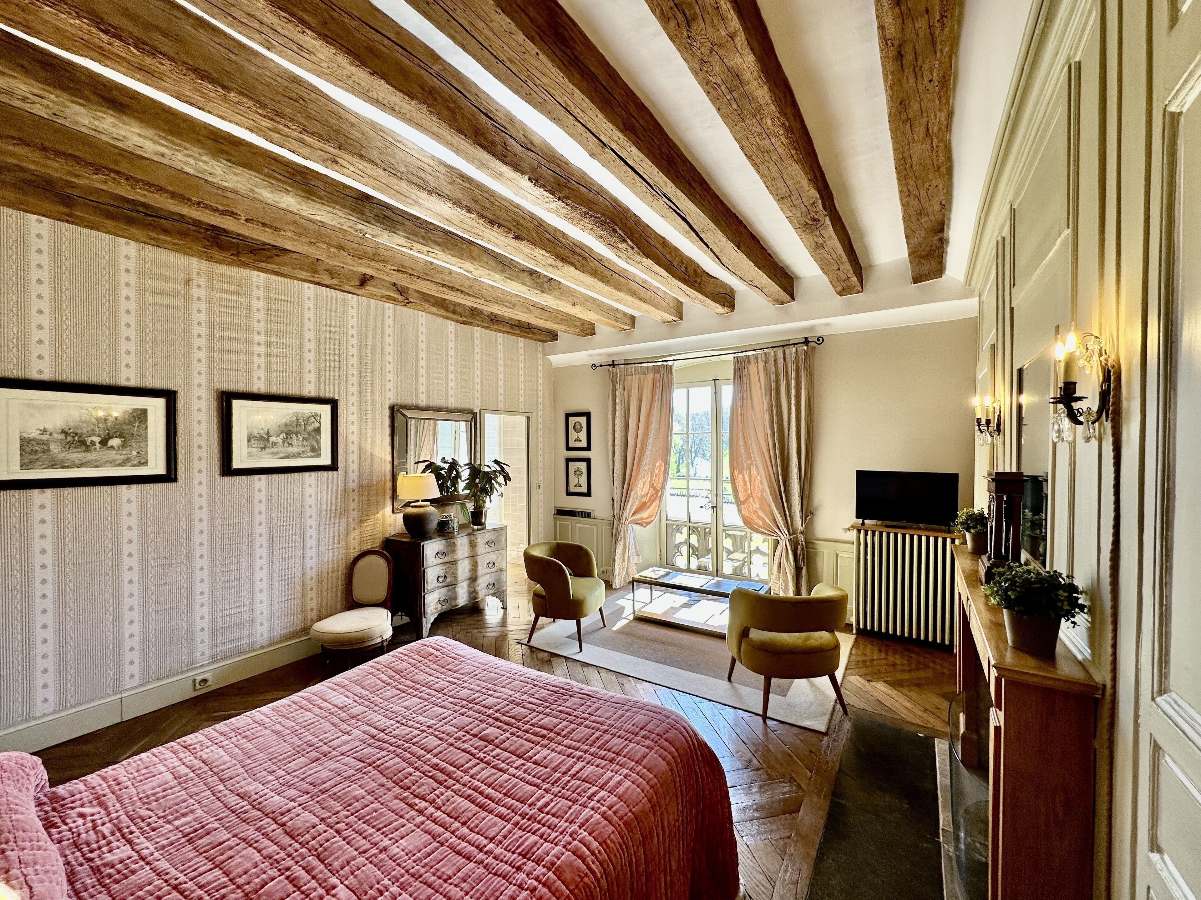 A hotel room with a large bed, a dresser, a TV, and a balcony with curtains.