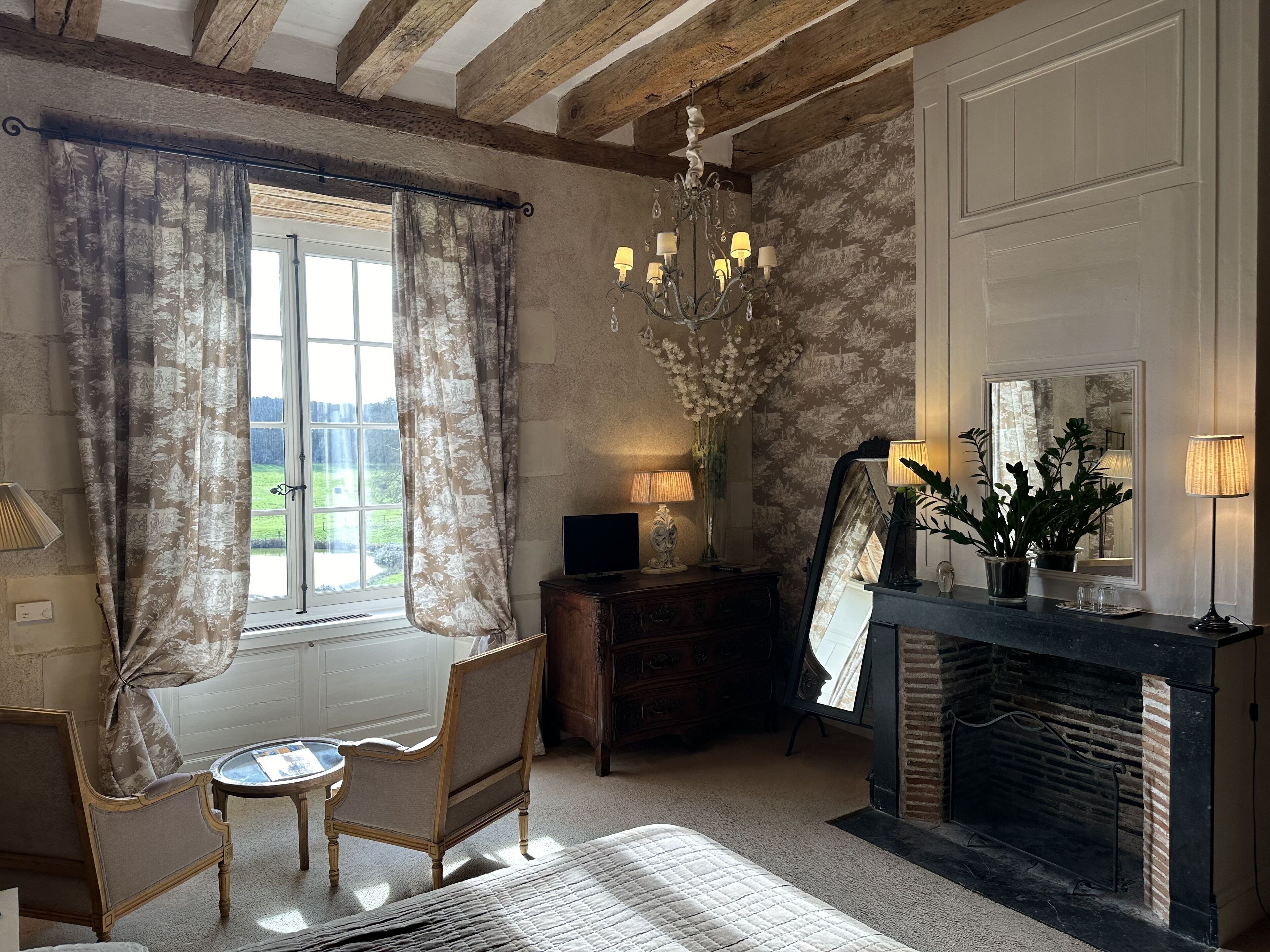 A room with a fireplace, a mirror, a chandelier, and a view of the outdoors.