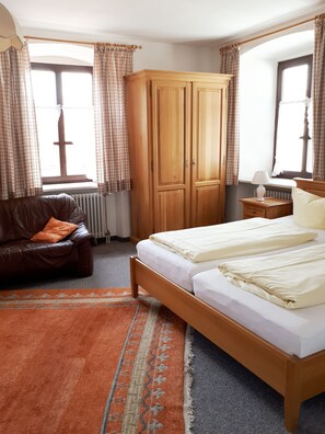 A bedroom with a wooden bed, a leather sofa, a wardrobe, and a window with curtains. - Gasthof zum Rassen (Garmisch-Partenkirchen)
