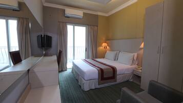 Habitación de hotel con cama, escritorio, silla, televisor, lámpara y armario.