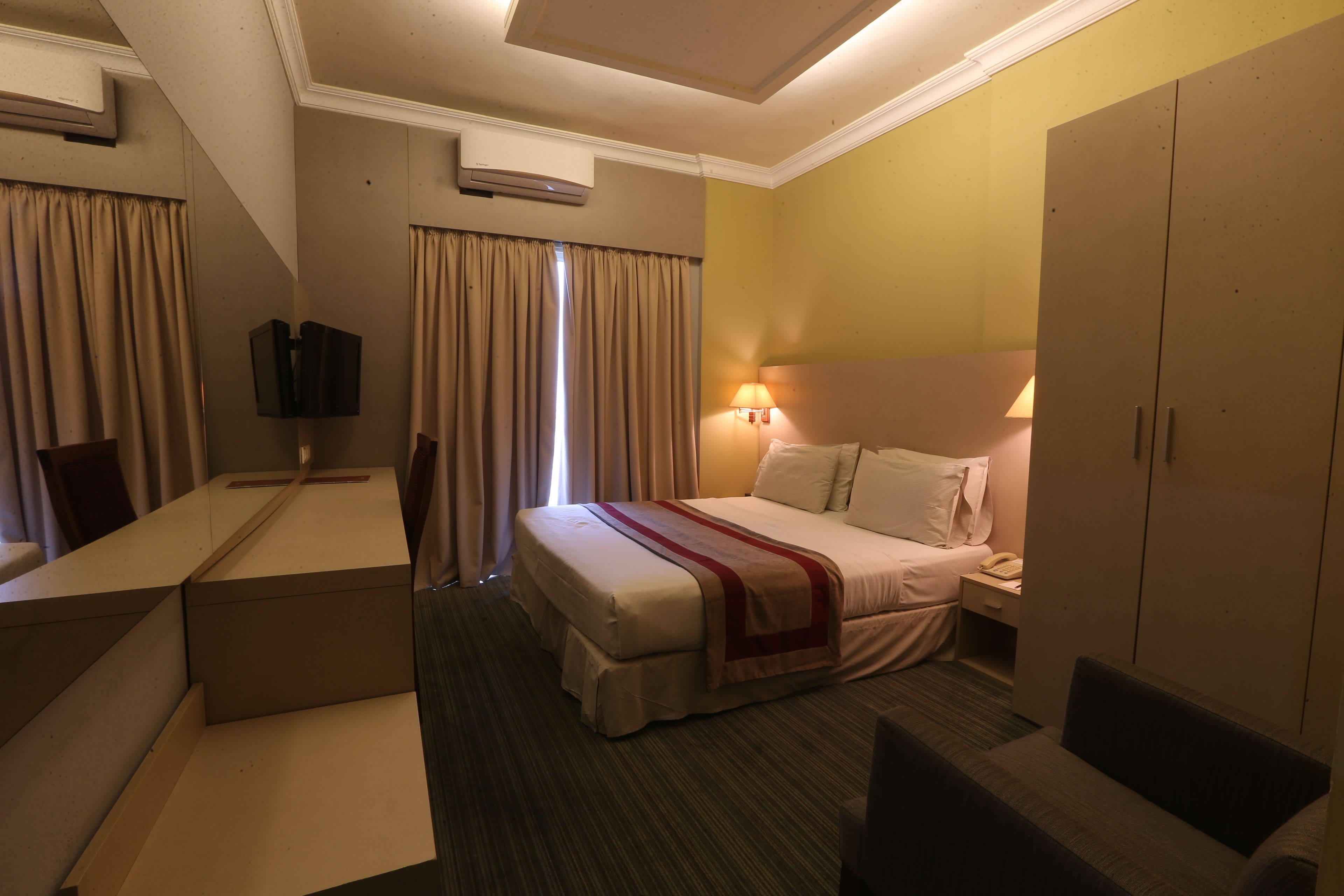 A hotel room with a bed, bedside table, lamp, wardrobe, and a TV.