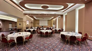 Un salón de conferencias con varias mesas redondas, sillas rojas y piso alfombrado.