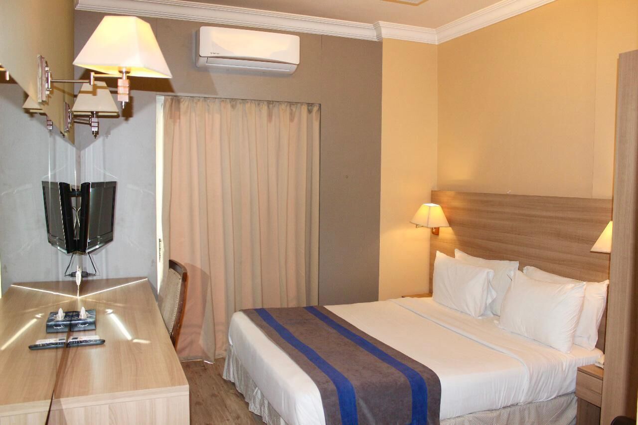 Habitación de hotel con cama, lámparas de noche, televisión y escritorio con controles remotos.