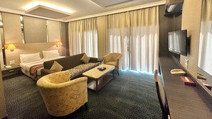 A hotel room with a bed, a sofa, a chair, a TV, and a window with curtains. - Padova Hotel (Sin El Fil)