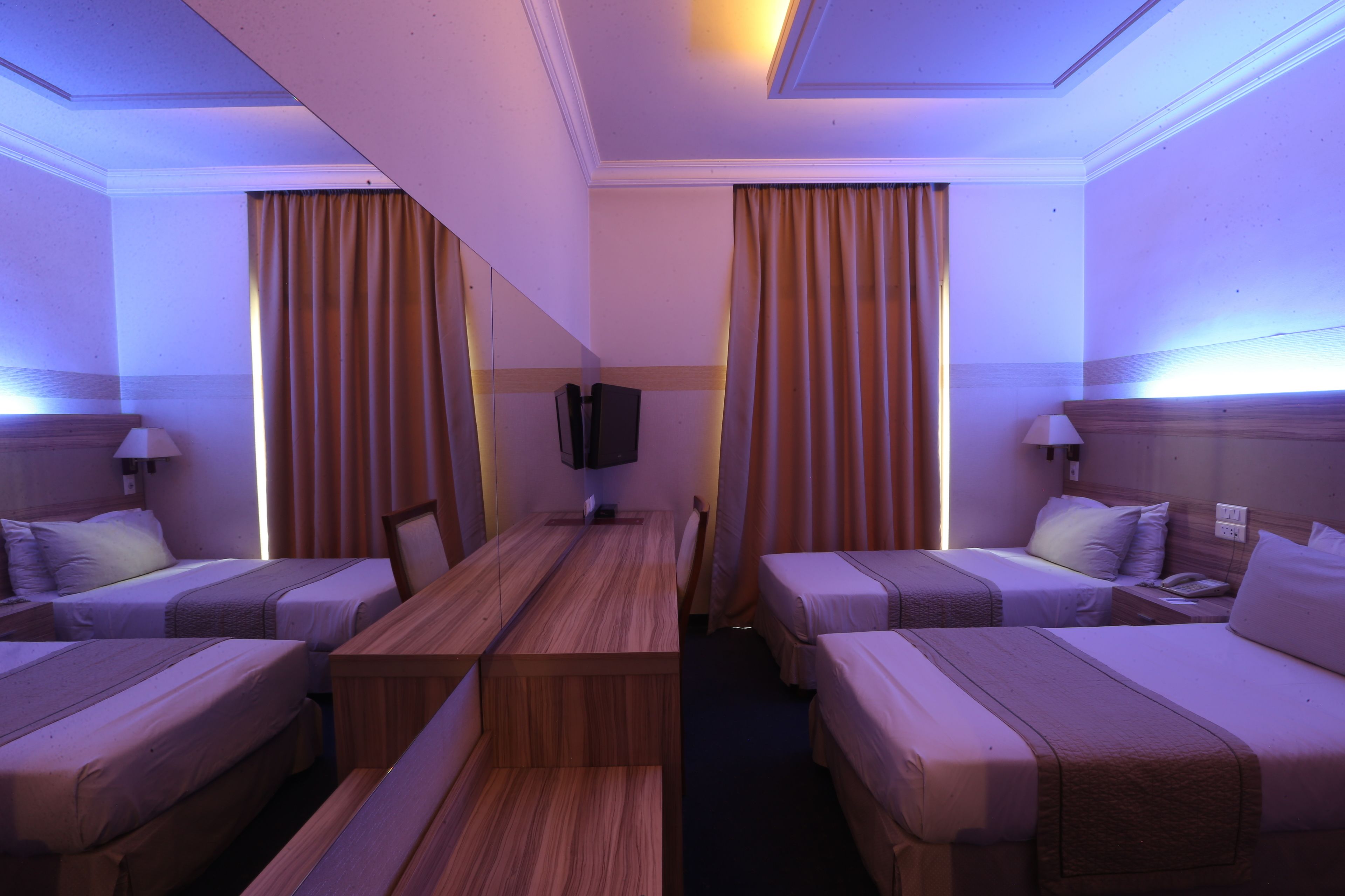 Quarto de hotel com duas camas de solteiro, uma mesa de madeira e uma televisão.