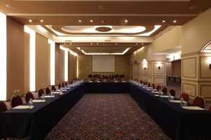 Un salón de conferencias con una larga mesa, sillas y una pantalla de proyector.
