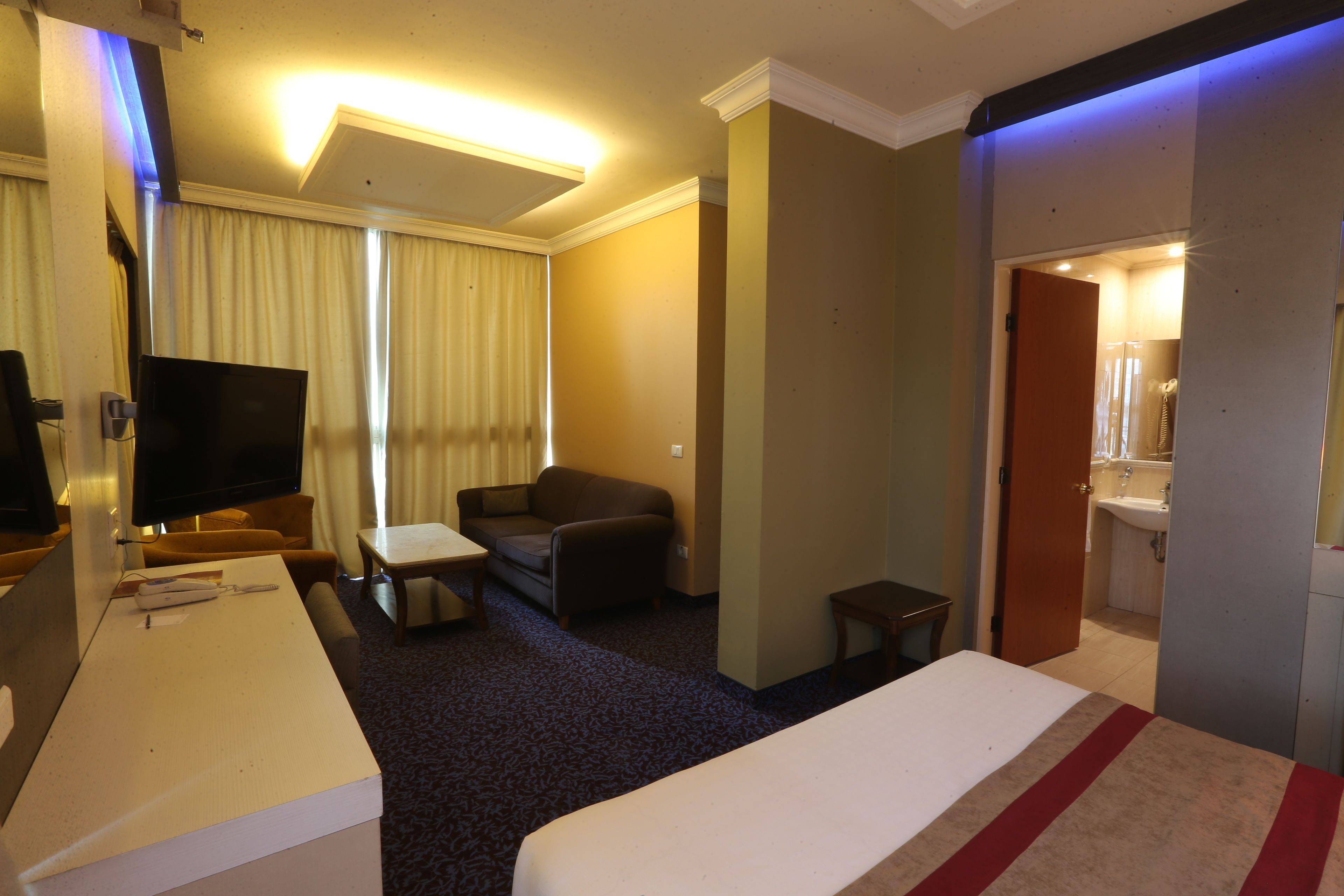 A hotel room with a bed, a desk, a television, a sofa, and a bathroom visible through an open door.