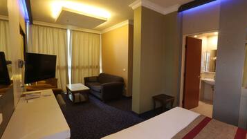 A hotel room with a bed, a desk, a television, a sofa, and a bathroom visible through an open door.