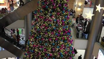 Un grand centre commercial à plusieurs étages, avec un sapin de Noël décoré et bien visible, orné d’objets colorés et surmonté d’une étoile.