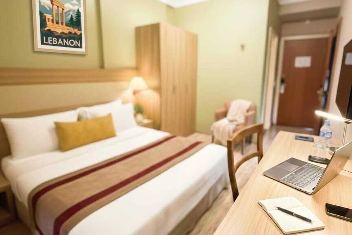 Habitación de hotel con cama, escritorio con una computadora portátil, una silla, armario y un cartel en la pared.