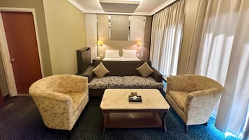 A hotel room with a bed, two armchairs, a coffee table, a desk, and a lamp.