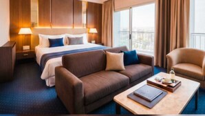 A hotel room with a large bed, a sofa, a coffee table, and a view of the city. - Padova Hotel (Sin El Fil)