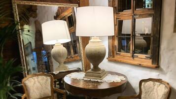 Una habitación con una mesa redonda de madera, dos sillas tapizadas, un espejo grande y una ventana con contraventanas de madera.