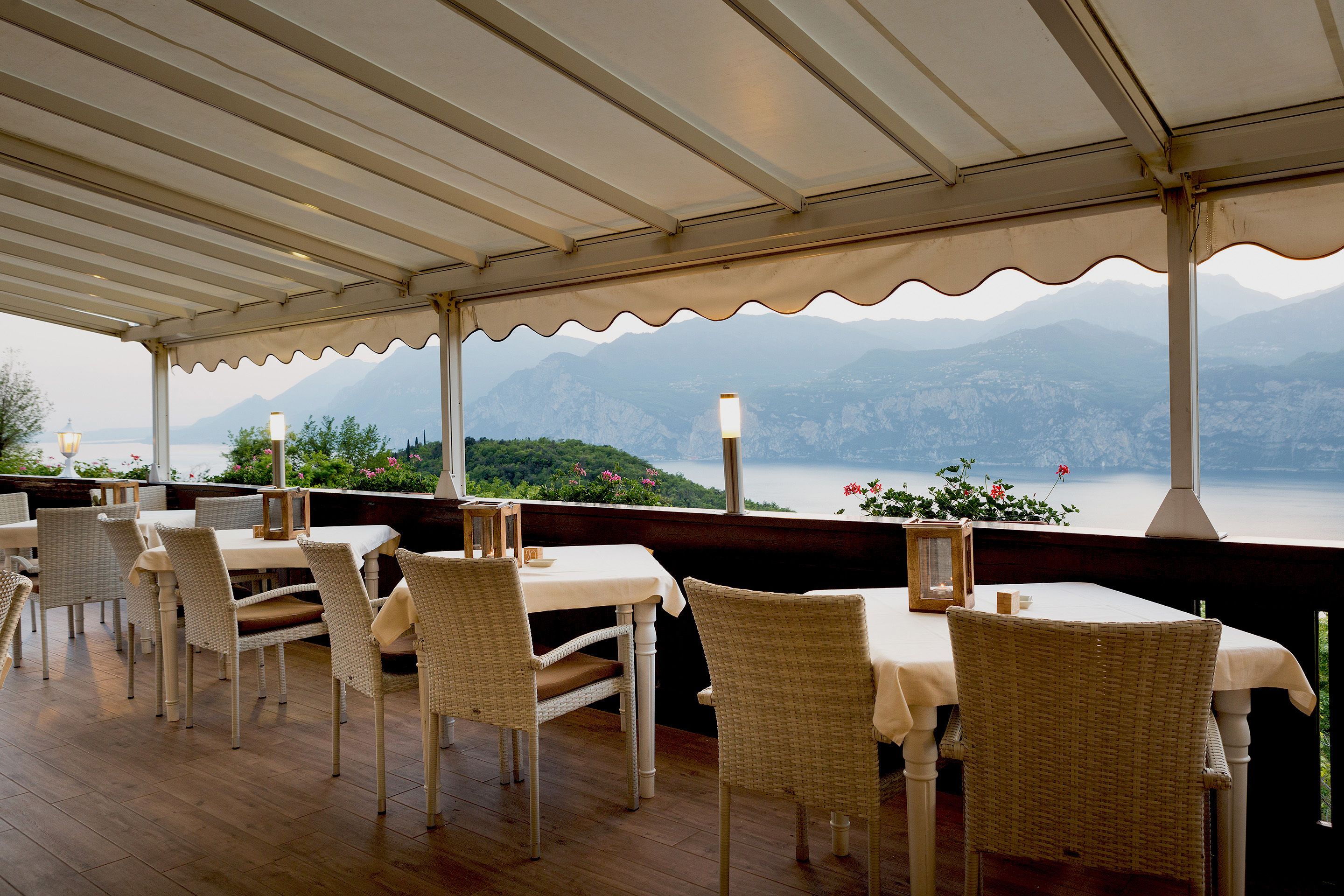 An outdoor dining area with wicker chairs and tables, overlooking a lake and mountains.