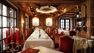 A long dining table set for a meal with candles, red chairs, and wooden beams on the ceiling.