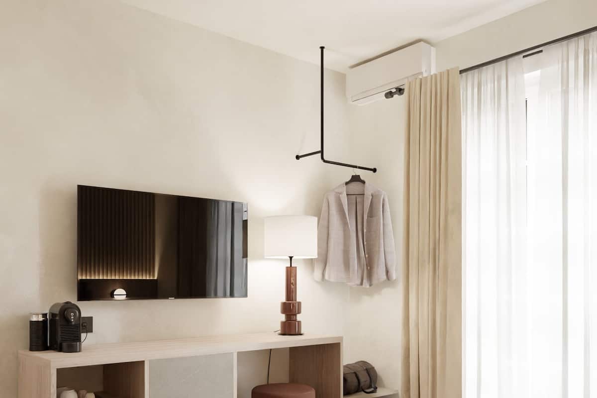 Una habitación de hotel moderna con una cama grande, un televisor de pantalla plana montado en la pared, un escritorio con lámpara y un armario.