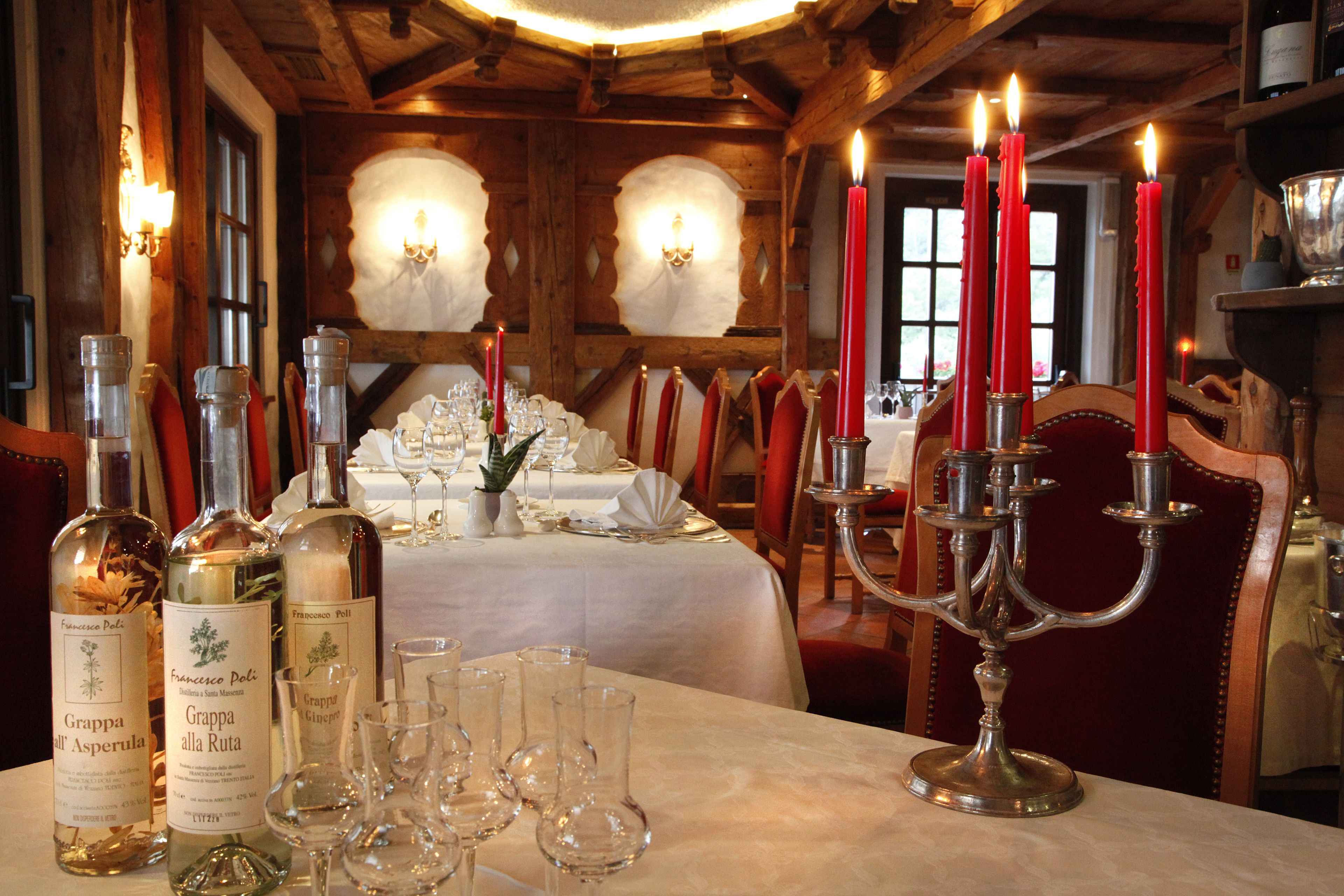 A dining table set with candles, wine bottles, and glasses in a warmly lit room with wooden beams and chandeliers.