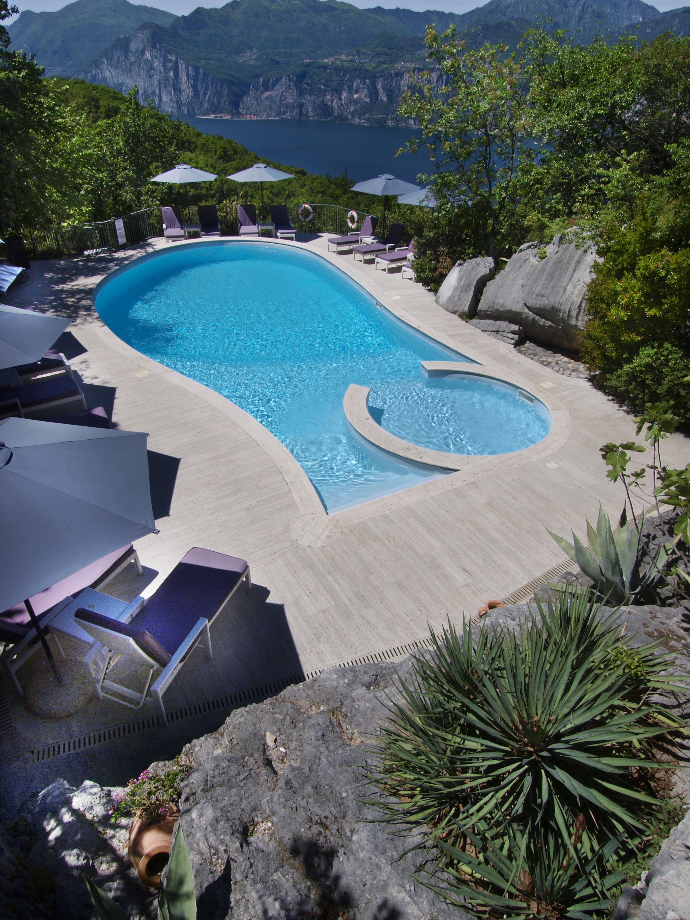 Una piscina con sillas de descanso y sombrillas, rodeada de vegetación y montañas al fondo.