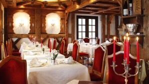 A dining area with wooden beams, white tablecloths, red chairs, and lit candles. - Hotel Querceto by Double Hospitality (Malcesine)