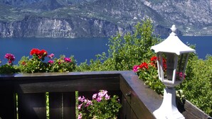 A wooden deck with a white lantern and flowers, overlooking a lake with mountains in the background. - Hotel Querceto by Double Hospitality (Malcesine)
