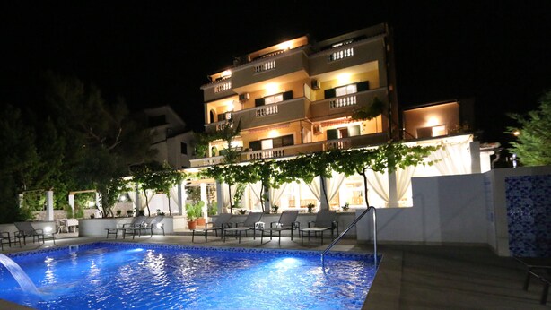 Une vue nocturne d’un hôtel doté d’une piscine, d’un espace extérieur aménagé et d’un immeuble à plusieurs étages avec des balcons.