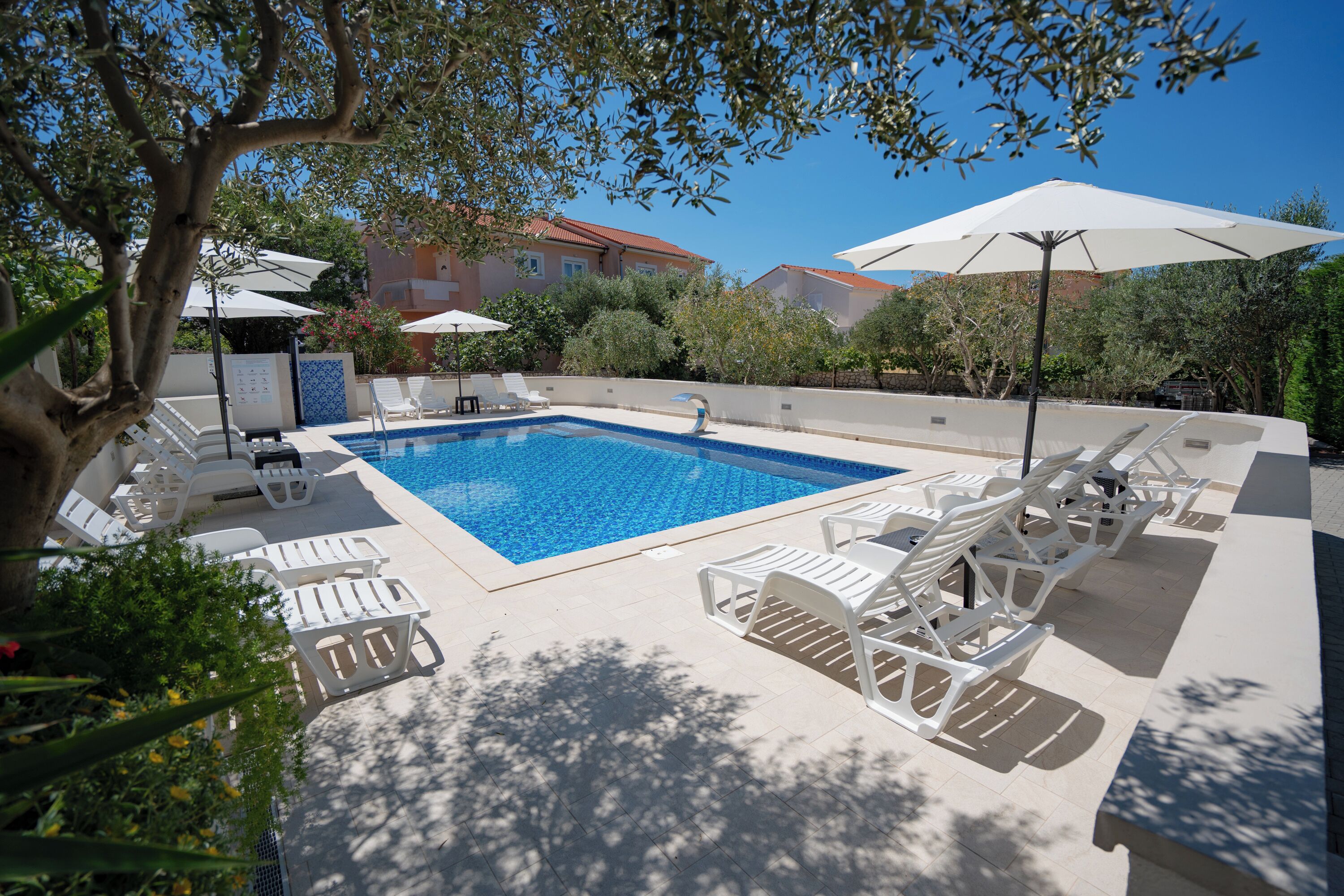 A swimming pool with lounge chairs and umbrellas, surrounded by trees and buildings.