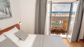 Une chambre d’hôtel avec un lit, une literie grise, un tableau au mur et un balcon avec vue sur la mer.