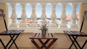 Un balcon avec des balustrades blanches, deux tables en bois et un plant de lavande en pot.