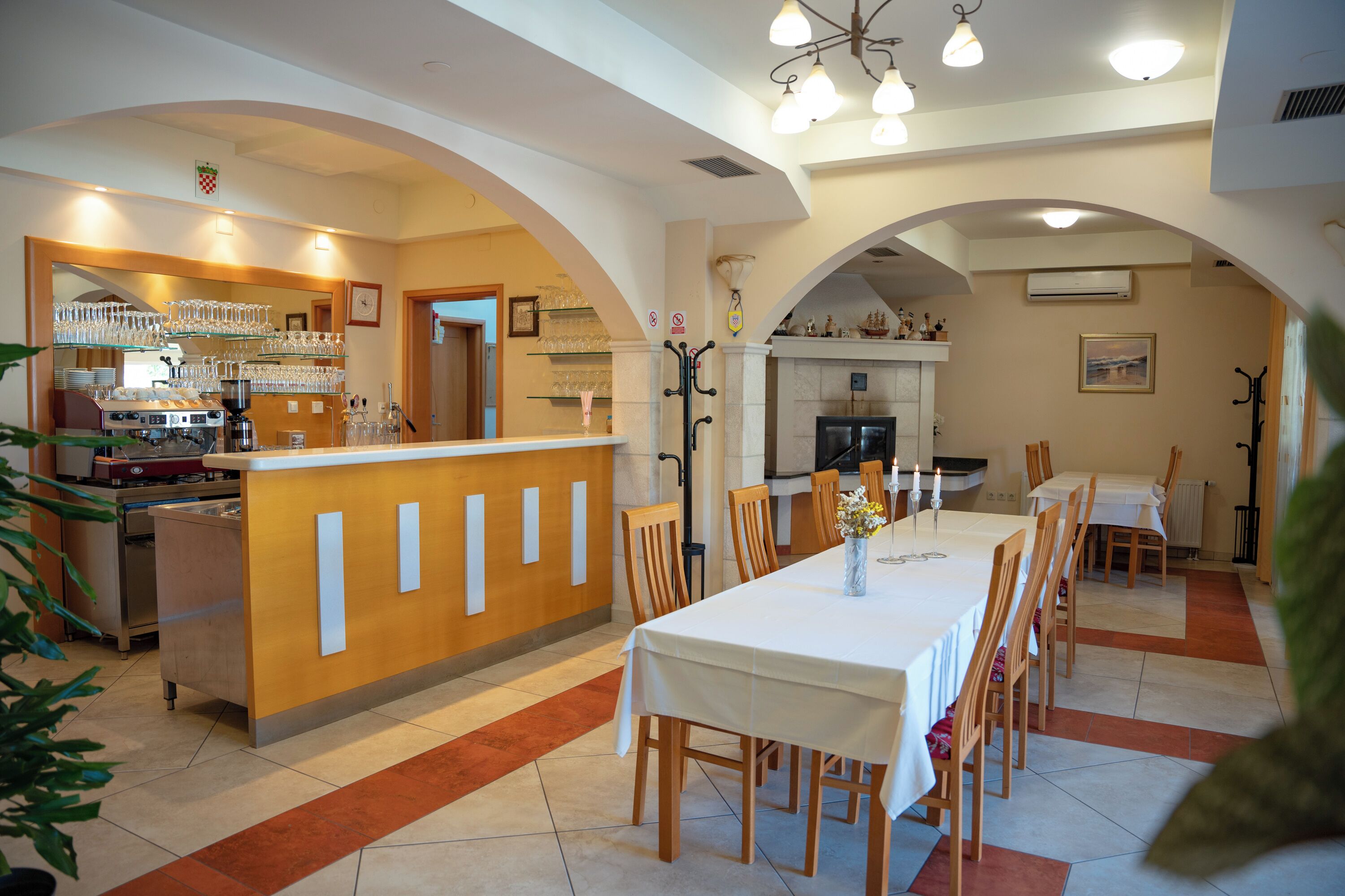 A restaurant with a long dining table, chairs, and a bar area with glassware.