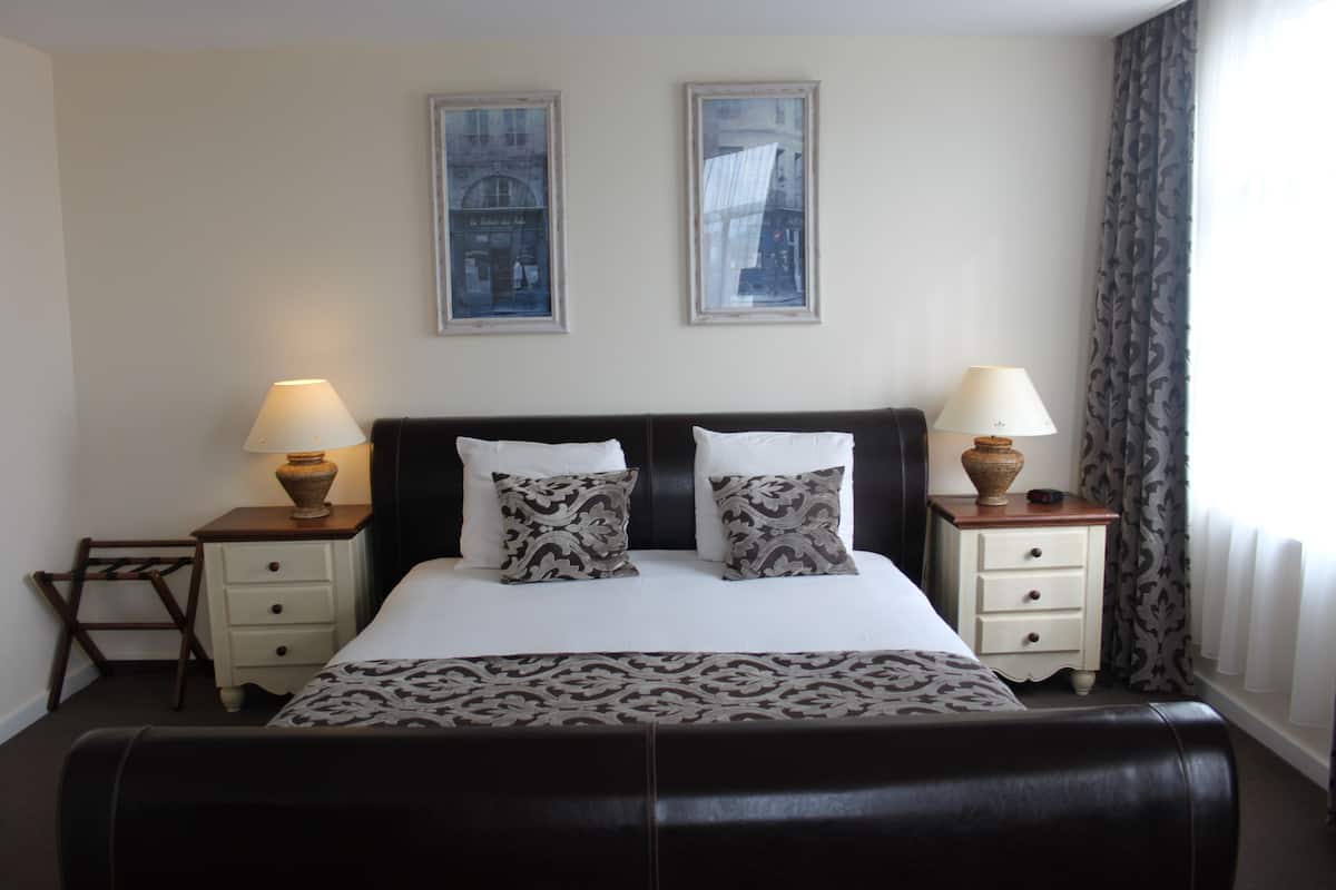 A neatly arranged hotel room with a large bed, two bedside tables with lamps, a chair, and two framed pictures on the wall.