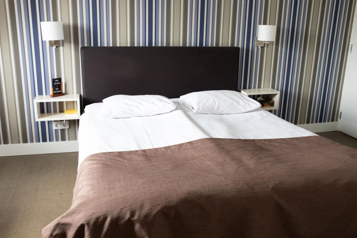 A neatly made bed with white and brown linens, two bedside tables with lamps, and a striped wall in the background.
