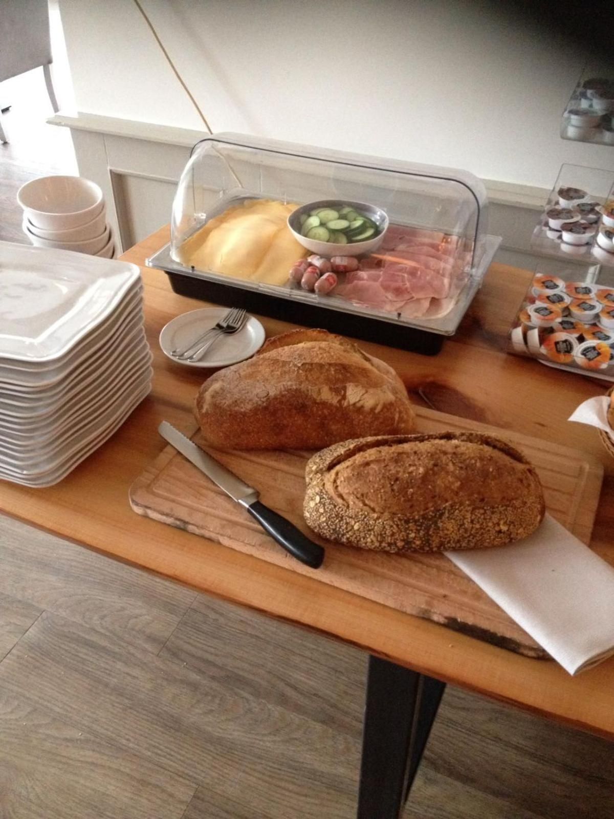 A table with a loaf of bread, a knife, a plate, a bowl of vegetables, and a tray of sliced meats.