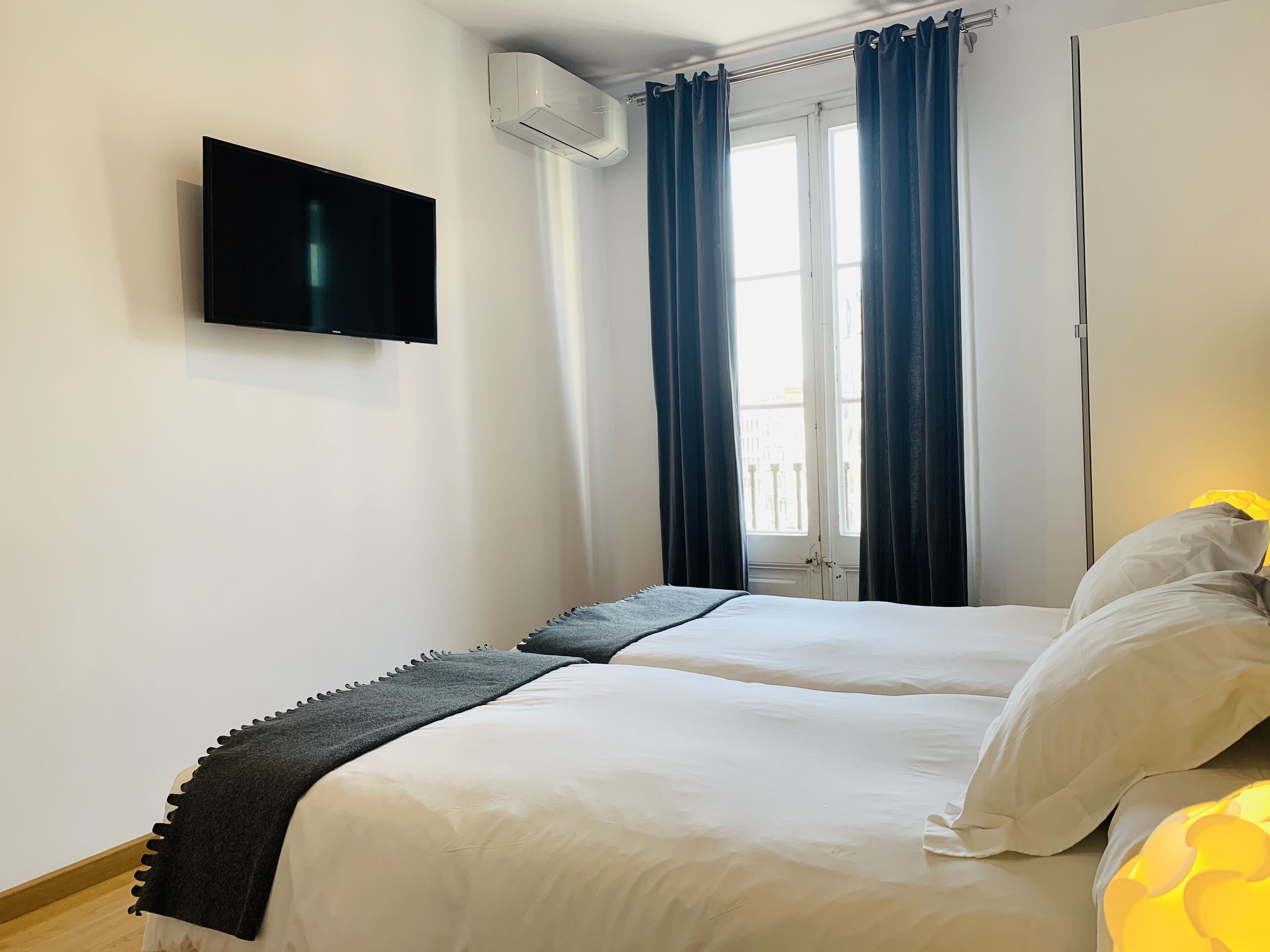 Een hotelkamer met twee bedden, een flatscreen televisie, een airconditioning en een raam met gordijnen.