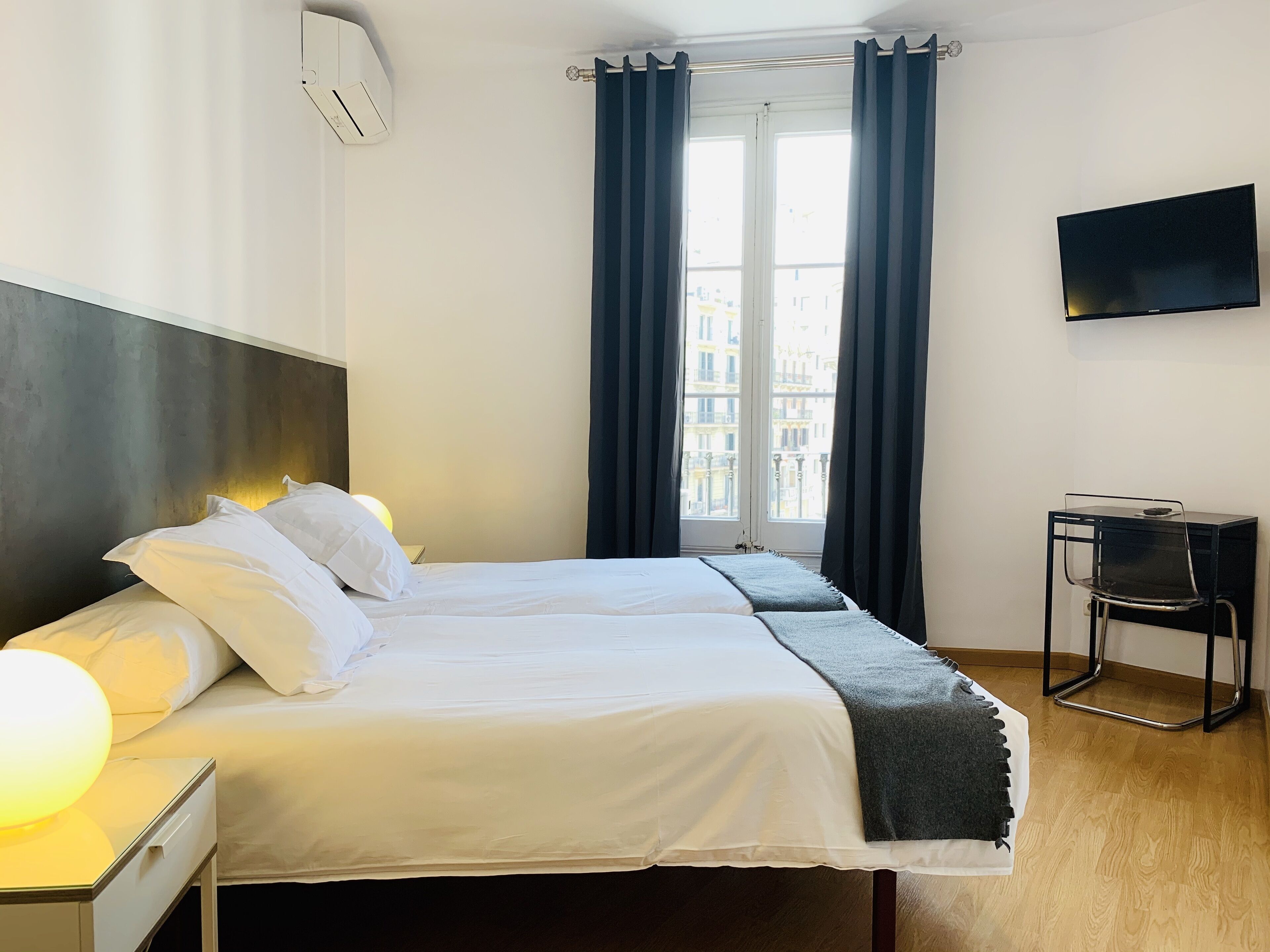 Een hotelkamer met twee bedden, een flatscreen televisie, een bureau met stoel en een raam met gordijnen.