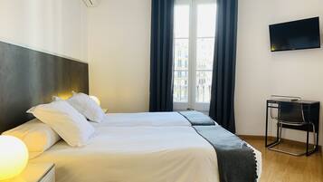 Een hotelkamer met twee bedden, een flatscreen televisie, een bureau met stoel en een raam met gordijnen.
