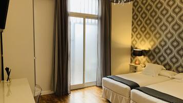 Habitación de hotel con cama, escritorio, silla, lámpara, pared con diseño y ventana con cortinas.