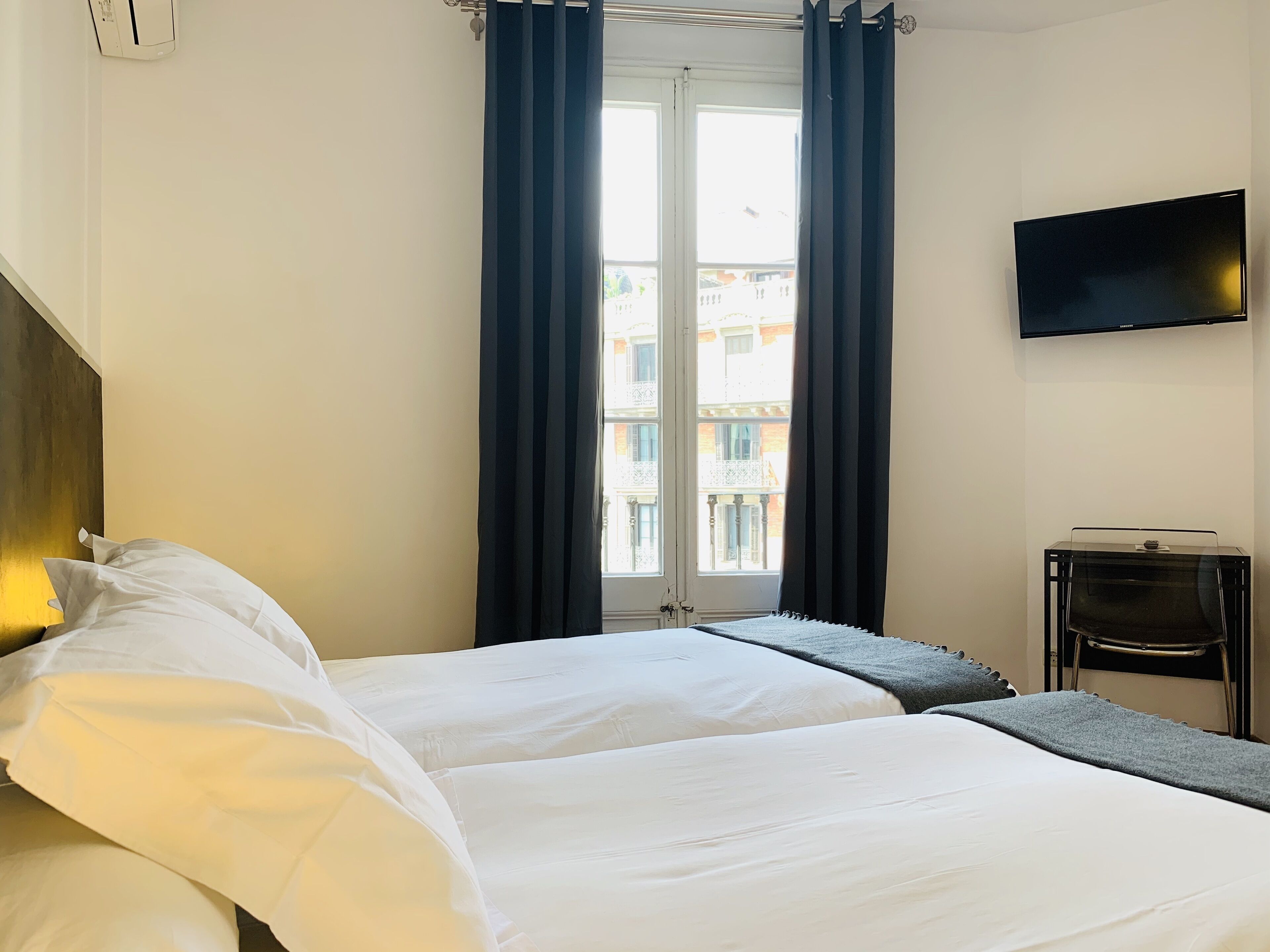 A hotel room with two beds, a TV, and a window with curtains.