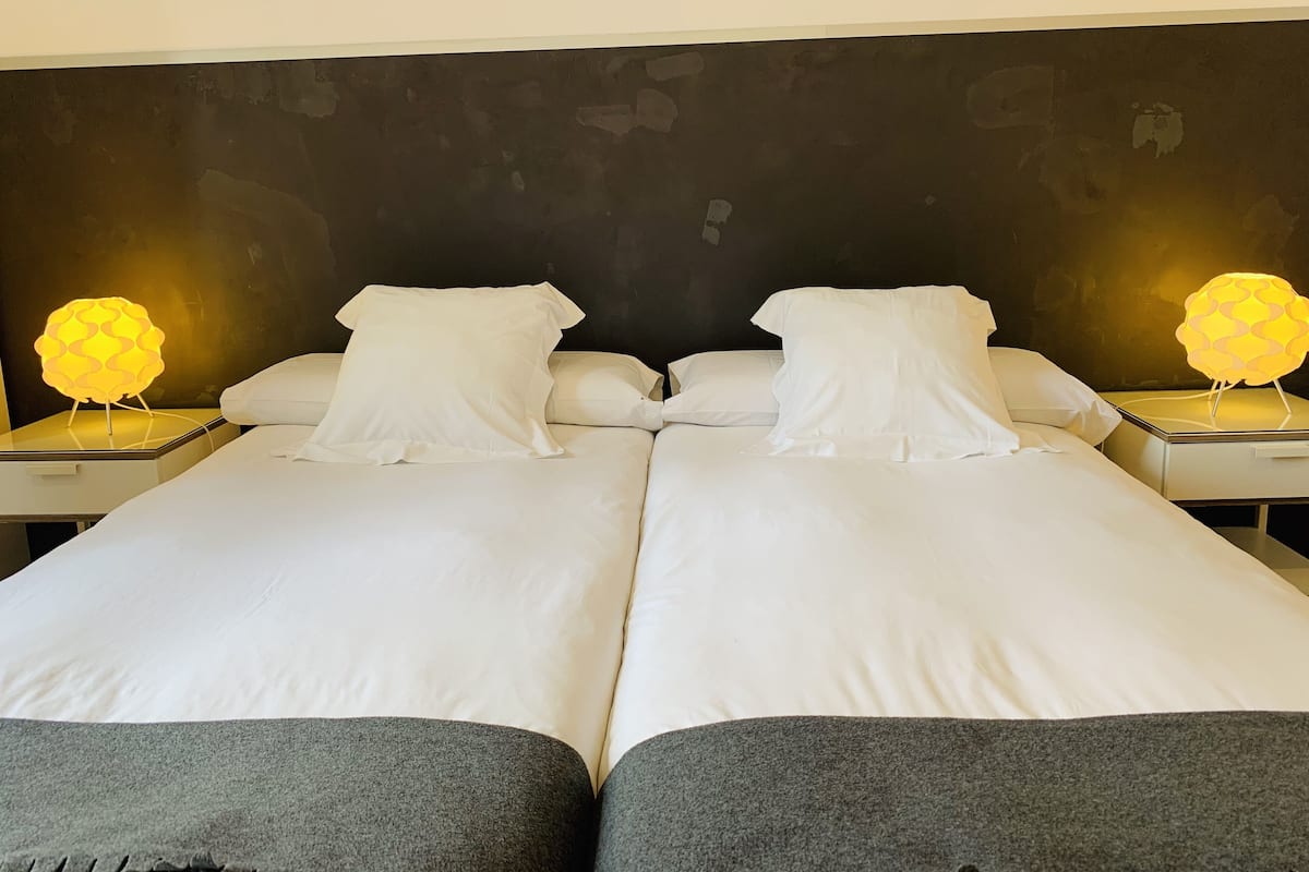 A double bed with white linens and gray footboards, flanked by two bedside tables with illuminated lamps.