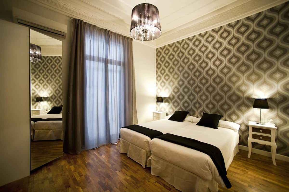 A hotel room with a large bed, two bedside tables with lamps, a mirror, and a patterned wallpaper.