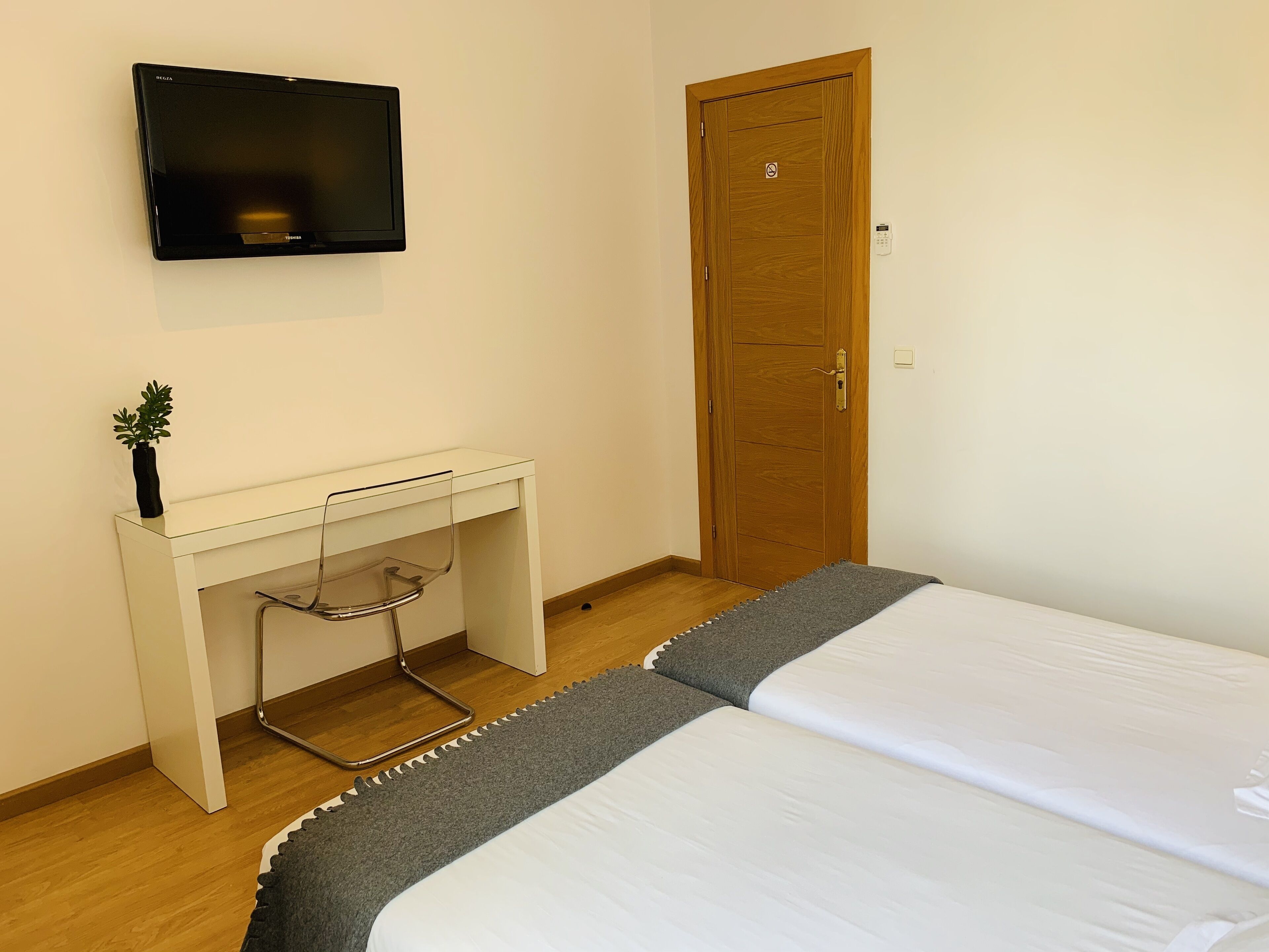 A bedroom with a bed, a desk, a television, and a door.