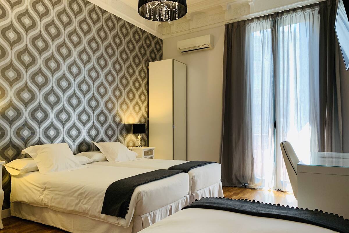 A hotel room with a bed, bedside table, lamp, wardrobe, and a window with curtains.