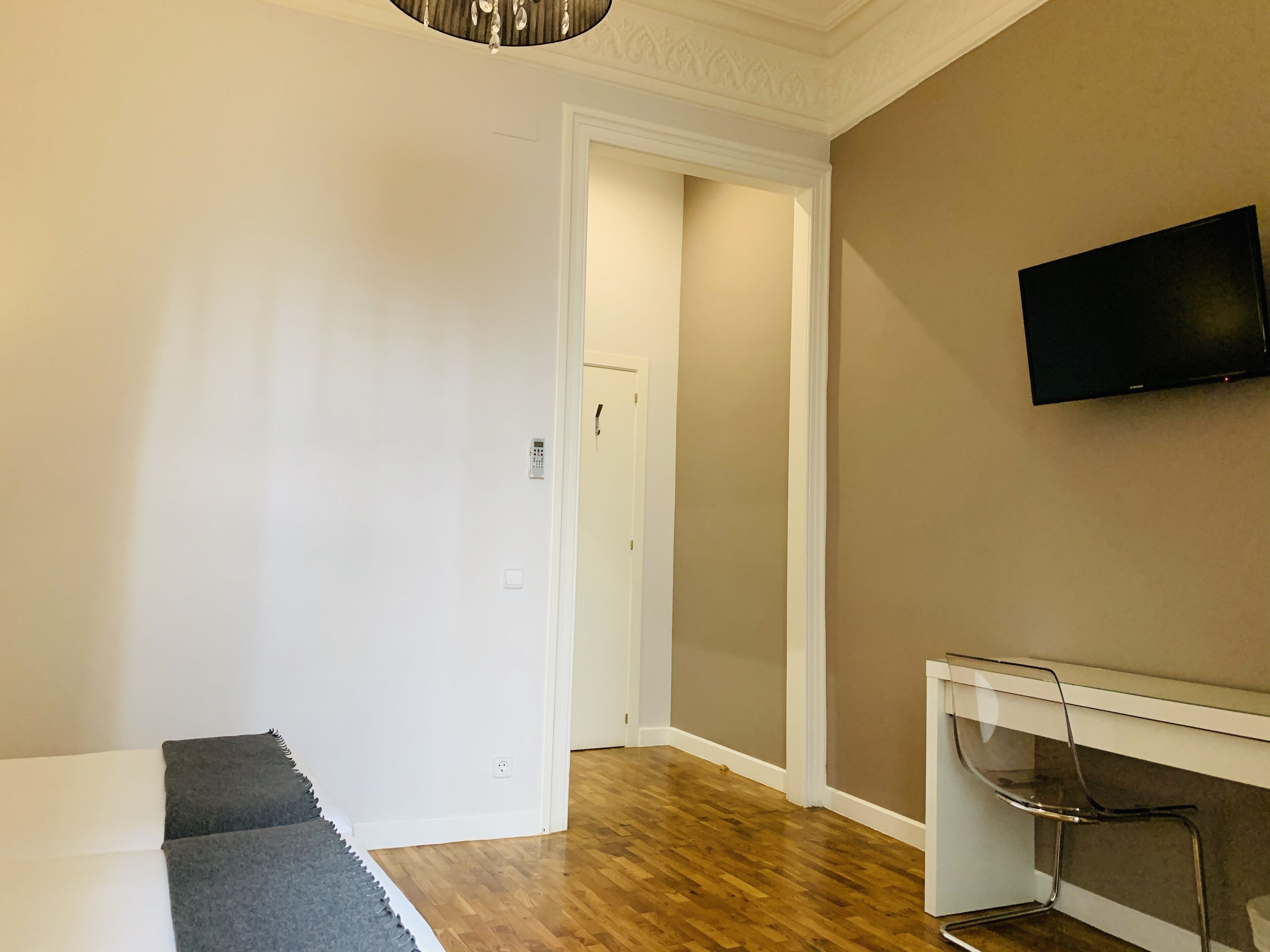 Une chambre moderne avec un plancher en bois, un mur blanc, un téléviseur fixé au mur et une petite table avec une chaise.
