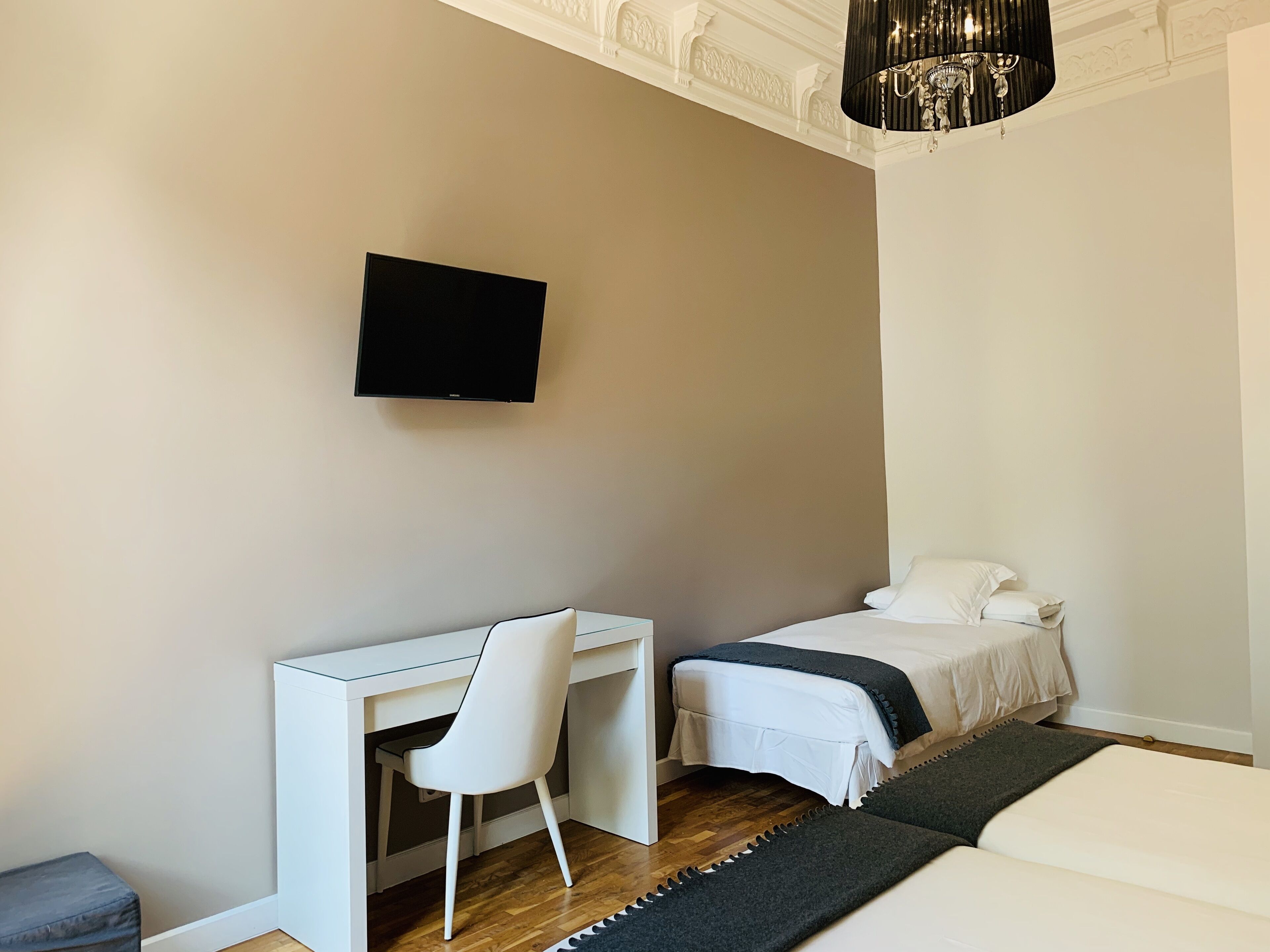 Une chambre moderne équipée d’un bureau, de deux lits, d’une télévision et d’un lustre.