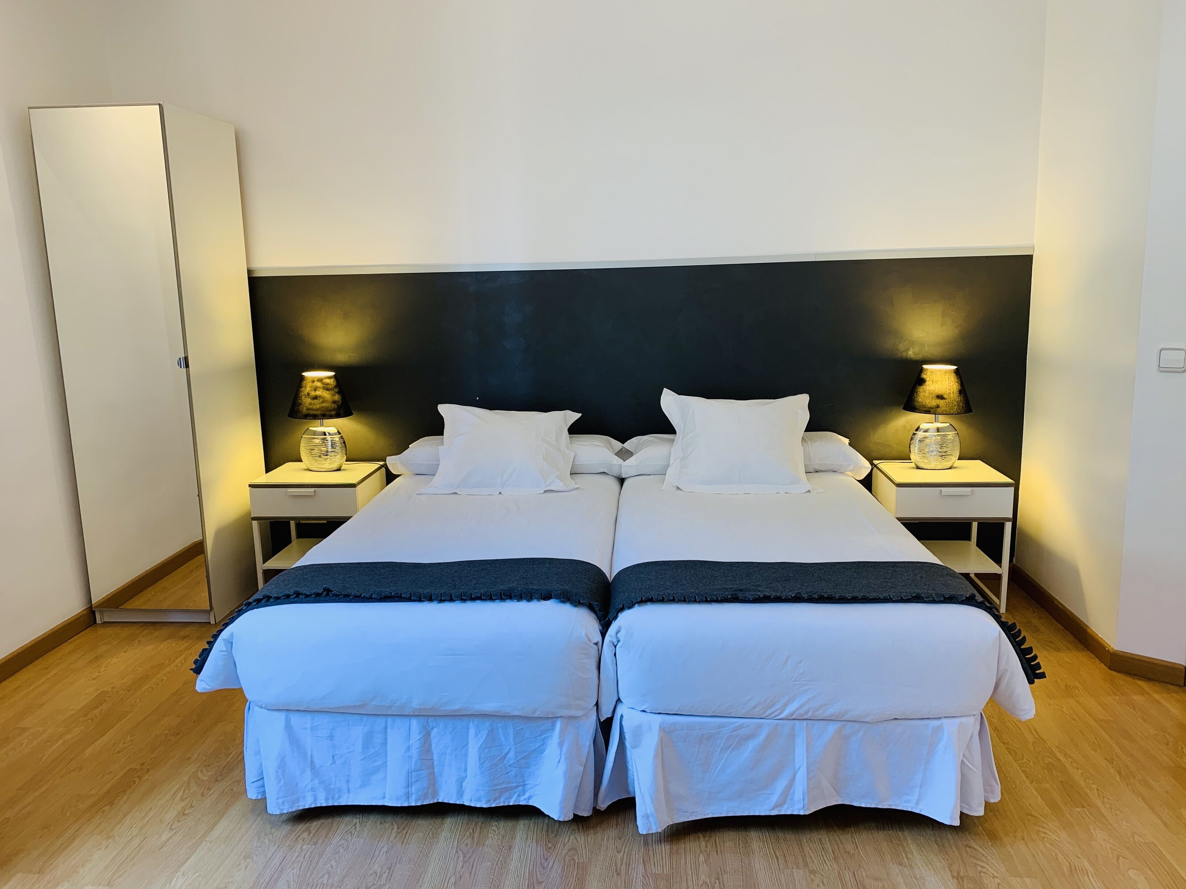Una cama doble con ropa de cama blanca, dos mesitas de noche con lámparas y un armario.