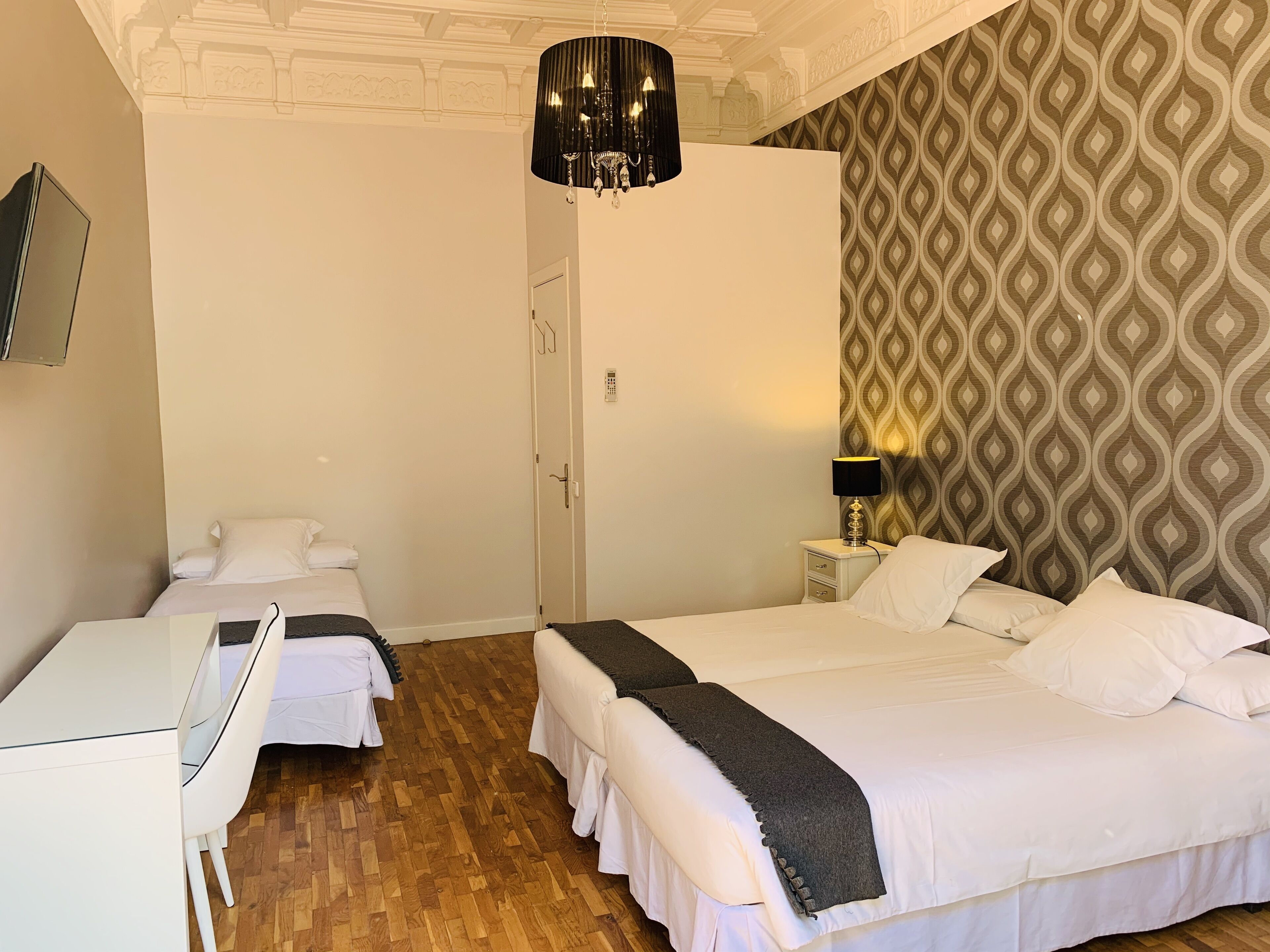Ein Hotelzimmer mit zwei Betten, einem Schreibtisch, einem Stuhl, einer Lampe und einer Wandtapete mit Muster.